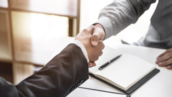 Dwie osoby uściskują dłonie, symbolizując zakładanie spółek przy biurku z notatnikami.