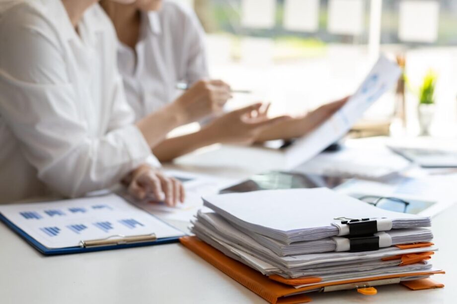 Stos dokumentów i dwie osoby omawiające szczegóły dotyczące usług księgowych.