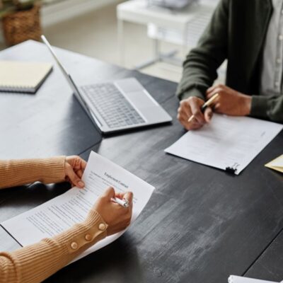 Dwie osoby siedzą przy stole z dokumentami, omawiając zakładanie spółek.