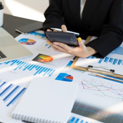 Księgowa pracuje nad dokumentami finansowymi z wykorzystaniem kalkulatora i laptopa.