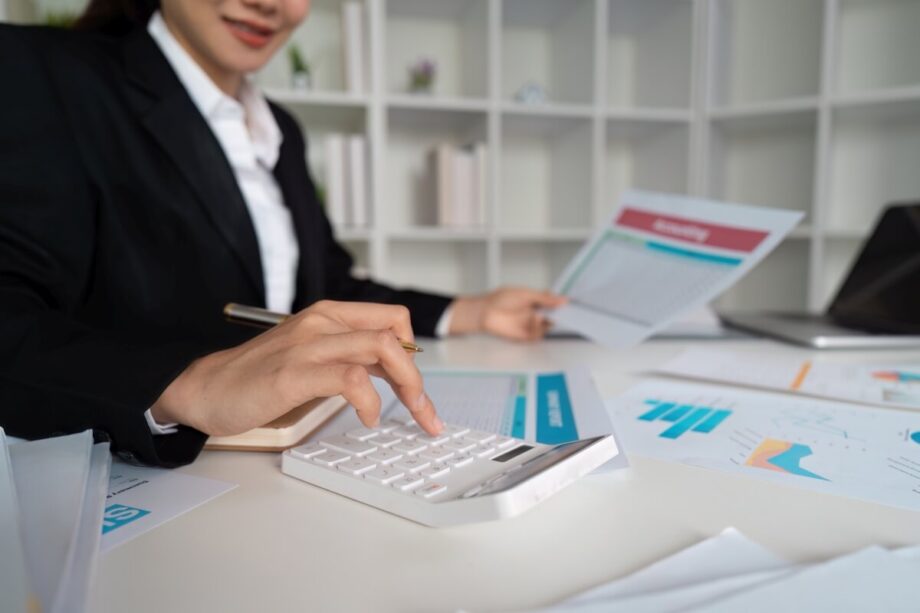 Osoba w garniturze wykonuje usługi księgowe przy użyciu kalkulatora.