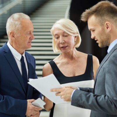 Trzy osoby w eleganckich strojach omawiają dokumenty jako pomoc w zakładaniu firmy.