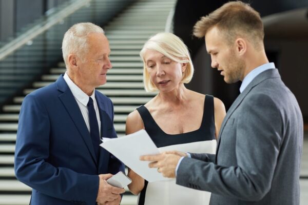 Trzy osoby w eleganckich strojach omawiają dokumenty jako pomoc w zakładaniu firmy.